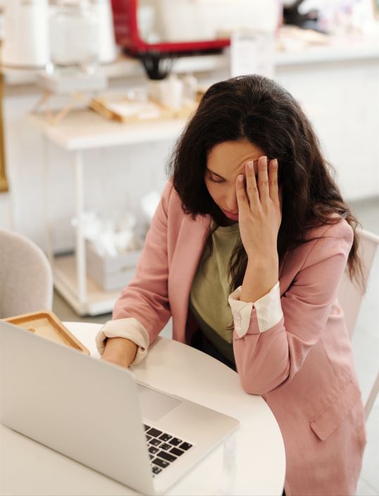 Female office worker sitting at laptop resting her hand on forehead with headache